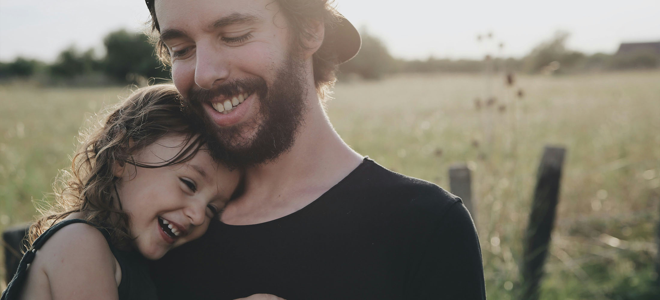 young dad cuddling child in field